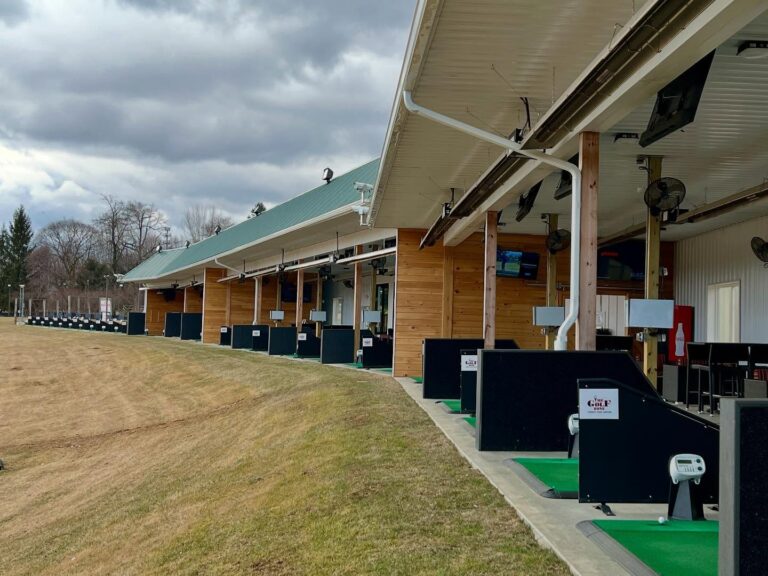 Golfers at Gravity Golf School in Pennsylvania, practicing their swings and receiving expert coaching in a picturesque golf course setting surrounded by lush greenery.